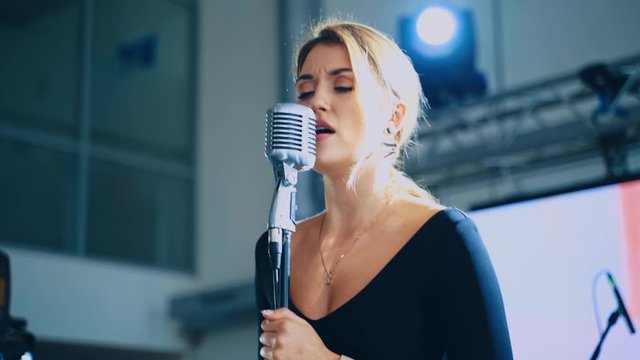 Blonde woman sings into the microphone. Attractive singer standing on the stage and singing a song. Musical entertainment.