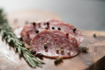 Sliced salame milano sausage on olive wood board with rosemary and pepper
