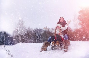 A winter fairy tale, a young mother and her daughter. A girl on a sled with gifts on the eve of the new year in the park. Two sisters walk in a New Year's park and ride a sled with gifts.
