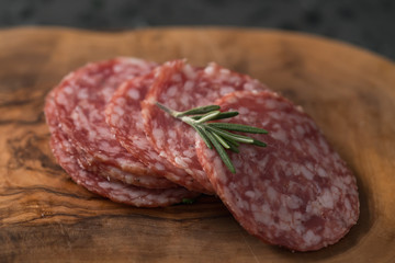 Sliced salame milano sausage on olive wood board with rosemary