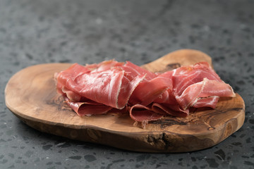 Sliced prosciutto ham on olive wood board