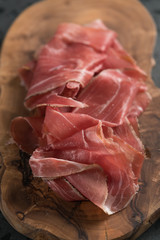 Sliced prosciutto ham on olive wood board