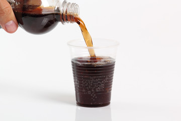 Human hand pouring cola from plastic bottle into disposable cup. Isolated on white background.