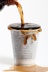 Pouring cola from bottle into overflowing plastic cup. Isolated on white background.