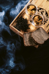 Chinese tea board with cups of hot green leaf tea Da Huan Pao and healthy cereal bread and prunes ready to serve. Close up menu tea ceremony for cafe or restaraunt