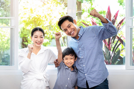 Asian Family, Including Father Mother And Daughter, Standing And Embracing In Front Of Glass Window At Home, Raise Hand With Cheerful