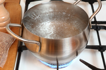 Boiling water into saucepan. Cooking buckwheat groats on gas stove.