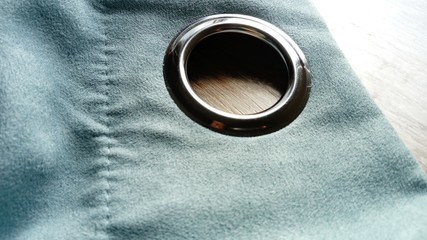 Metal grommet on a gray-blue velvet curtain. The fabric lies on a wooden table. The hole on the...