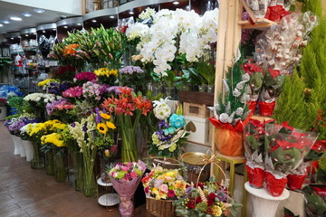 Bouquet of colorful roses and other different flowers at the entry to flower shop at farmers' market. Colorful peony, roses etc. Pots with flowers on the shelf of plant shop. Dubai UAE December 2019