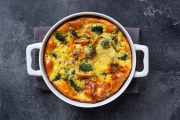 Baked omelet with broccoli in a ceramic dish. Dark concrete table. Copy space. Healthy diet food dish.