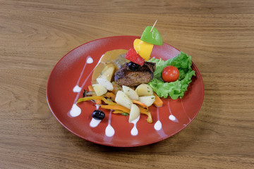 Restaurant food served on a red plate. Fish, cheese, salad, vegetables, sauce.