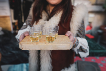 Shallow depth of field (selective focus) image with a woman holding a wooden plate with palinca (or...
