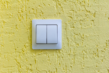 A white light switch on a yellow concrete wall.Turn the lights on or off.