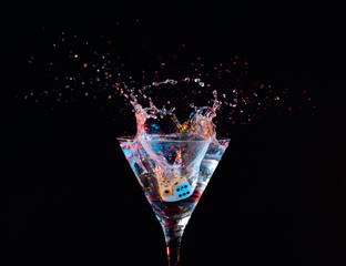 Dice fall in a glass of martini. Colourful cocktail in glass with splash.