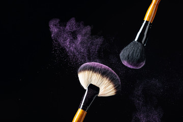 Makeup concept with a  professional makeup brushes with glowing purple eye shadow isolated on black background.