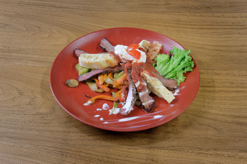 Restaurant food served on a red plate. Fish, cheese, salad, vegetables, sauce.