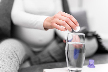 Pregnant woman taking vitamin tablet in a glass of water.