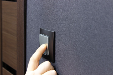 Turn off the light! The finger presses the button of the black wall switch in the room. The concept...
