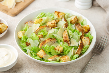 traditional Caesar salad with lettuce, roasted chicken,  croutons and cheese in white bowl