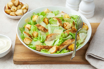 traditional Caesar salad with lettuce, roasted chicken,  croutons and cheese in white bowl