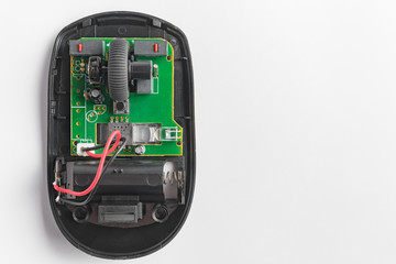 The broken internal parts of the wireless mouse for computer are open for repair. Circuit board and electronic parts on white background.