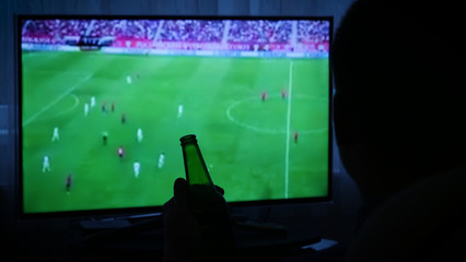 Young man watching football on television with beer bottle, Man Relaxing near TV.