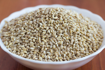 Pearl barley in a white plate on the table, close-up.
