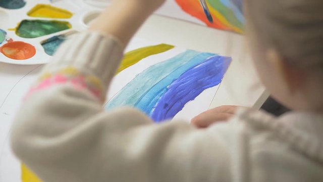 the left-handed girl draws a rainbow with watercolor paints and brushes, children's joint creativity.
