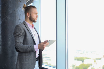 Handsome young businessman holding digital tablet while standing near the window.