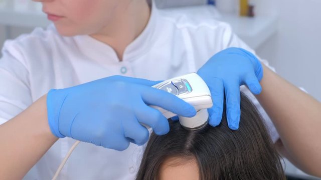 Doctor trichologist examines woman patient's hairs using dermatoscope in clinic, hands closeup. Dermatologist is working in clinic on modern equipment. Medicine and healthcare concept.