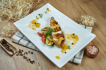 Appetizing baked chicken breast with cheese, vegetables and sweet sauce on a white plate. Diet food. Close up. Flat lay