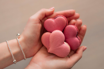Woman hands holding many pink macaroons in the heart shape