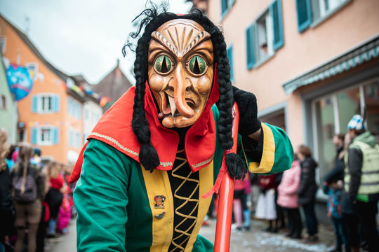 Freiburger Hexen - Hexe mit Katzenaugen im  gr&uuml;n, gelb, rotem Gewand mit schwarzen Z&ouml;pfen und krummer Nase. Bei Fastnachtsumzug in Staufen S&uuml;d Deutschland.