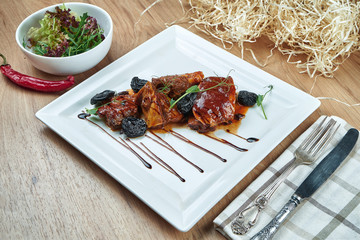Appetizing pork baked in sweet and sour sauce and prunes on a white plate. Close up view. Tasty food for lunch