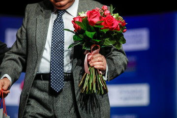 Shallow depth of field (selective focus) image with a senior man receiving a bouquet of flowers and a present during a ceremony.