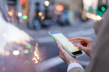 Closeup photo of female hands holding modern smartphone with blank screen. Mockup ready for text message or content. Woman's hands with cellphone. Empty display. Night street, bokeh light