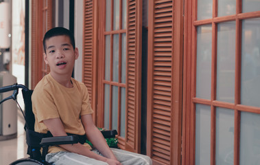 Asian special child on wheelchair is smile happily on wooden door background, Life in the education age of disabled children, Happy disabled kid concept.