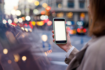Closeup photo of female hands holding modern smartphone with blank screen. Mockup ready for text message or content. Woman's hands with cellphone. Empty display. Night street, bokeh light