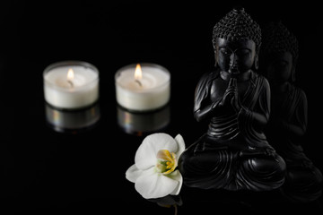 Buddha with burning candles and orchid on black background