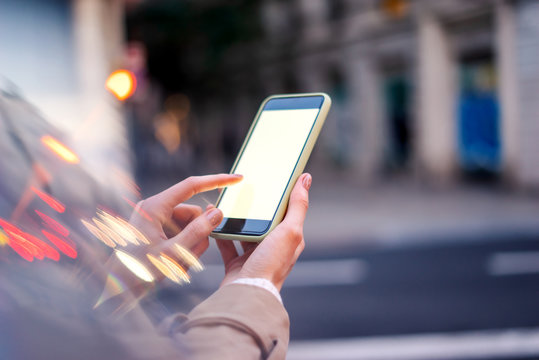 Closeup photo of female hands holding modern smartphone with blank screen. Mockup ready for text message or content. Woman's hands with cellphone. Empty display. Night street, bokeh light