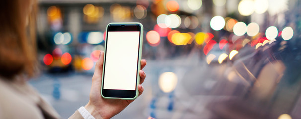 Closeup photo of female hands holding modern smartphone with blank screen. Mockup ready for text message or content. Woman's hands with cellphone. Empty display. Night street, bokeh light