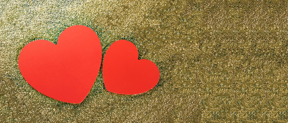 Red hearts on a golden glitter background, wide view with a copyspace.