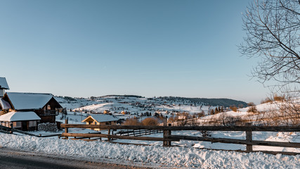 Winter season, landscape picture of a village covered by snow at sunset, country landscape with timber fence