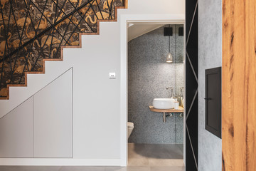 Corridor with stairs and open door to elegant bathroom with silver wall and white sink