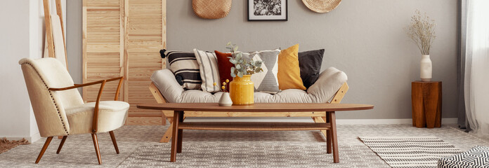 Wooden and wicker accessories in fashionable scandinavian living room interior with futon sofa with pillows