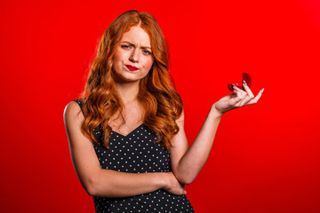  Disappointed upset girl, she doesn't like gift. Pretty european young woman in polka dot dress holding small jewelry box with marriage proposal on red background.