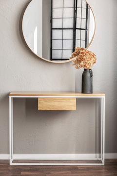 Elegant Round Mirror In Wooden Frame Above Fancy Console Table With Flowers In Vase In Trendy Bedroom Interior With Beige Vase