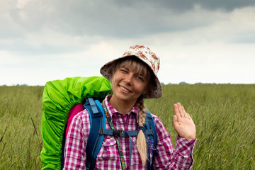 Young beautiful woman with a backpack on a hiking trip, in a cheerful mood, crosses a meadow.