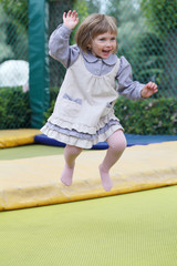 Fototapeta premium Little girl on playground in a park, jumping on trampoline Little Girl on a Trampoline.