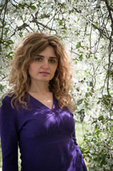 soft focus of beautiful confident woman in purple blouse looking at camera in front of blooming tree in garden